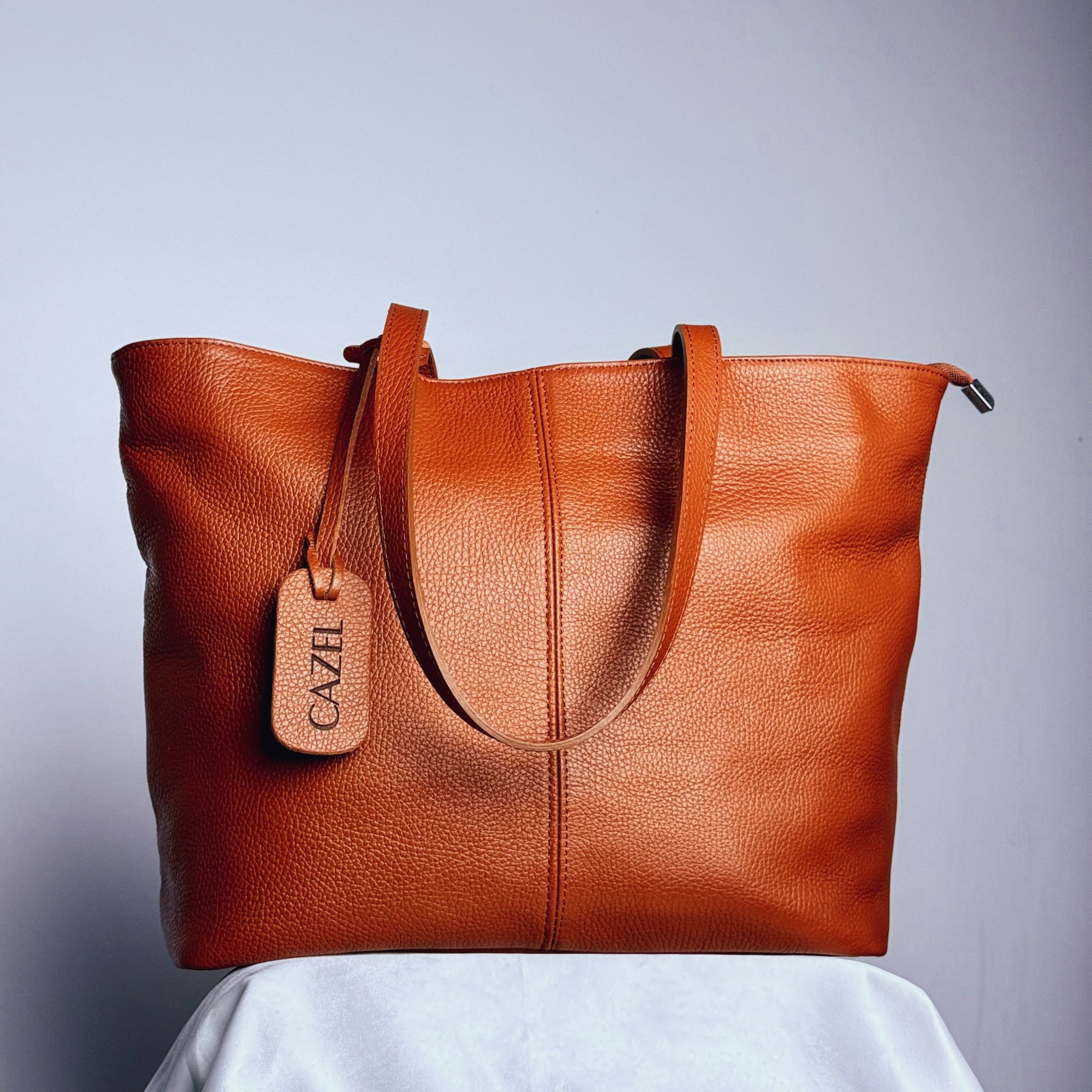 Brown leather tote bag with a visible brand tag on a light gray background